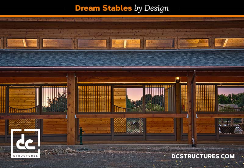 A modern horse stable design with large windows at the upper level showcases a warm, illuminated interior. The structure features sliding doors with metal grills and a DC Structures logo at the bottom left corner. Text reads "Dream Stables by Design.