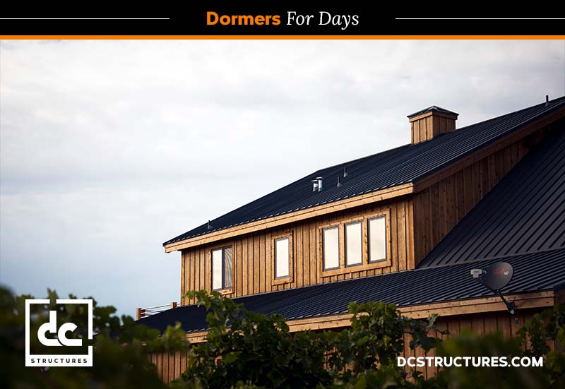 A wooden barn home with a black metal roof features several dormer windows. The sky is overcast, and the foreground has some greenery. The text reads, "Dormers For Days," and "DC Structures" is visible at the bottom.