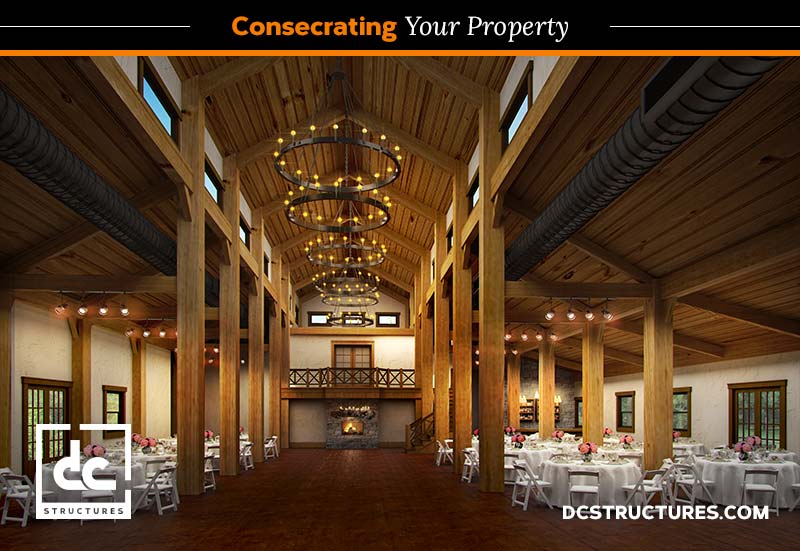 The interior of the rustic barn-style event space, crafted from a wedding barn kit, boasts high wooden ceilings, prominent beams, and elegant chandeliers. Tables are set for a formal occasion. A large fireplace and wooden balcony enhance the ambiance while branding for DC Structures is visible.