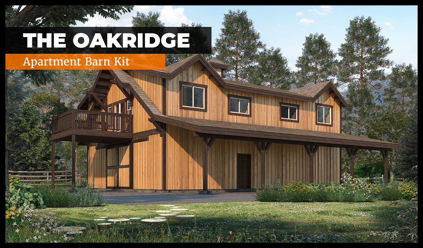 A rustic barn with a wooden exterior and large windows, surrounded by trees and greenery. A sign reads "The Oakridge Apartment Barn Kit." The building features a balcony and is set against a backdrop of a forested area under a clear sky.