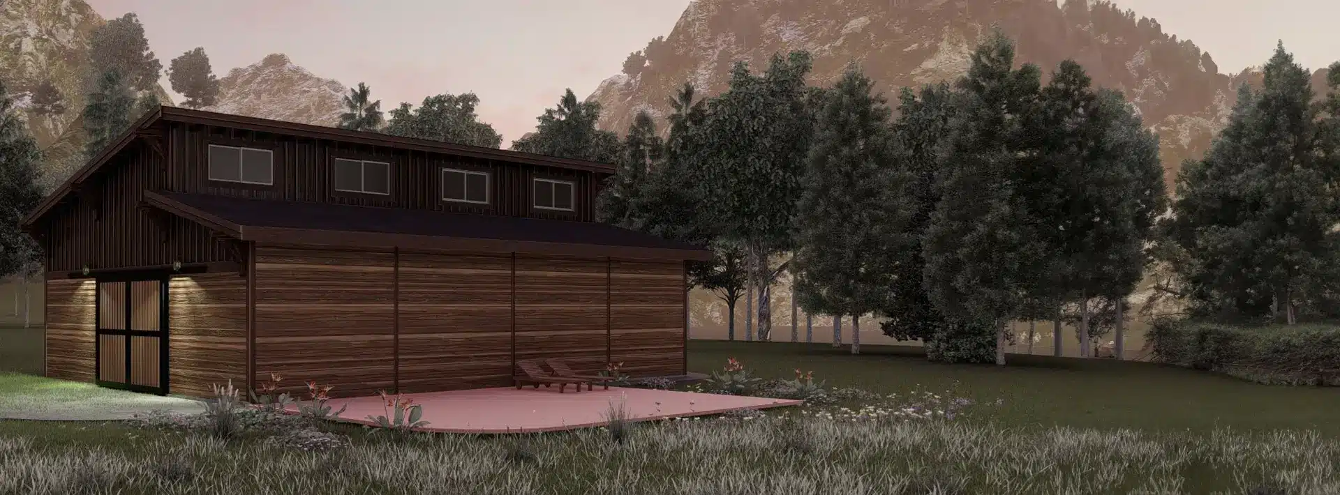 A modern wooden cabin with large windows and an outdoor patio sits in a grassy clearing surrounded by trees and mountains at sunset.