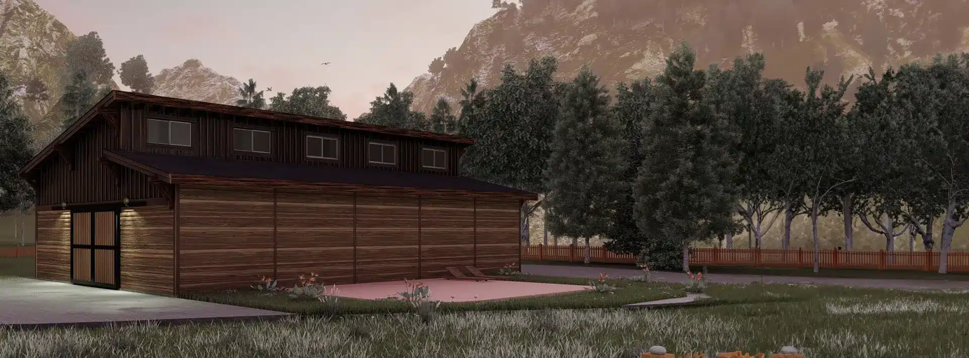 A modern wooden barn-like building stands next to a grassy lawn, surrounded by tall pine trees, with a mountain in the background at sunset.