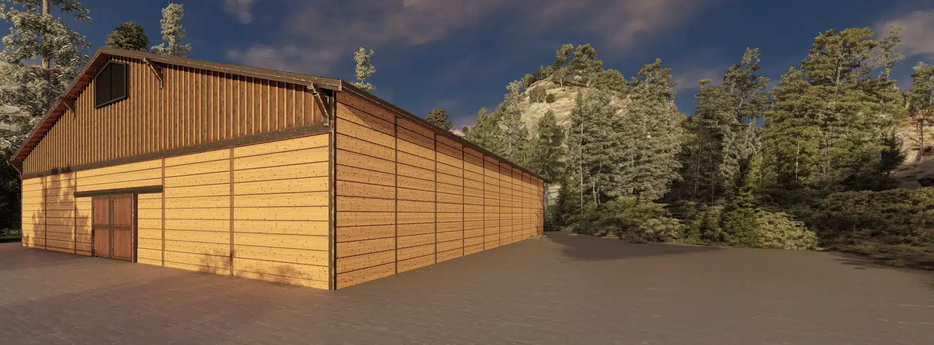 A large, light-colored wooden barn sits on concrete, surrounded by dense trees and rocky hills under a blue sky with clouds.