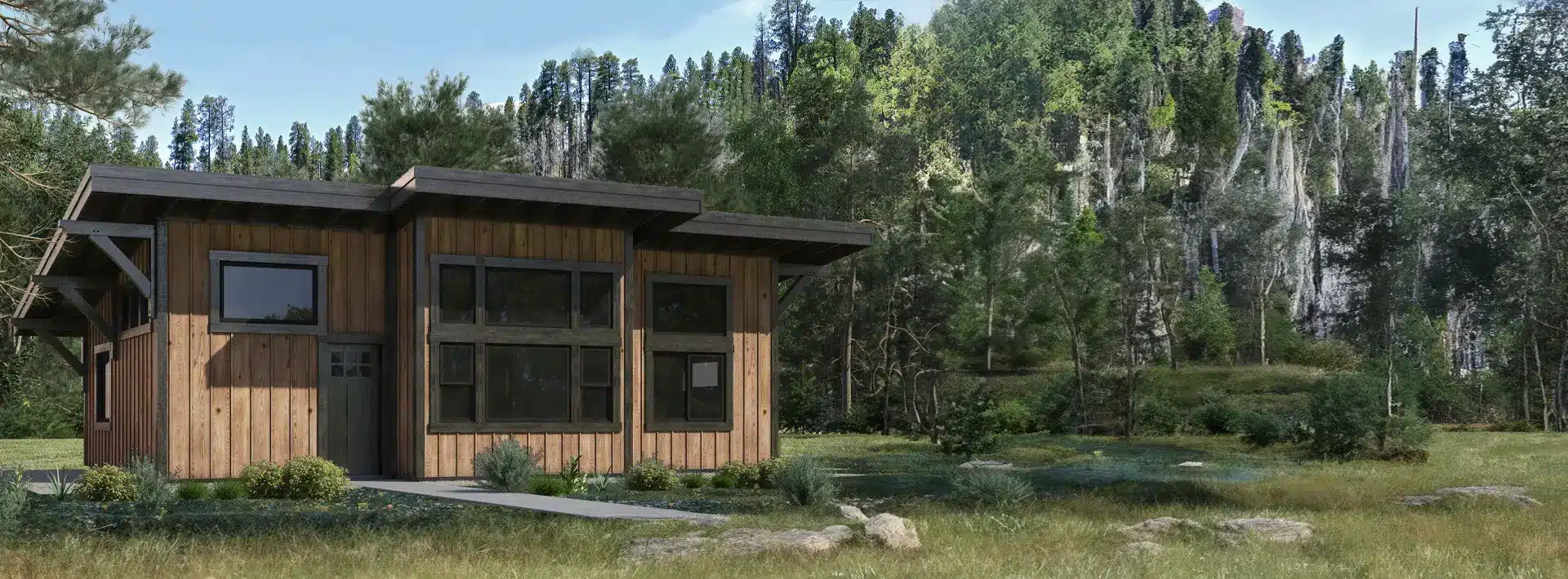 A small modern wooden cabin with large windows sits in a grassy clearing, surrounded by pines, cliffs, forest, and blue sky.