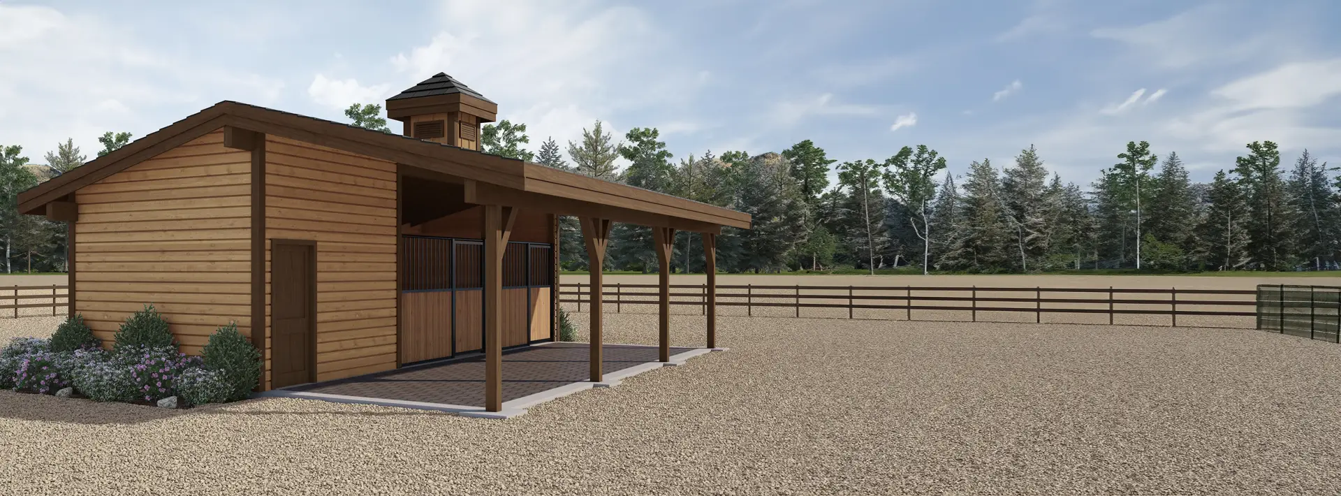 A wooden barn with a covered porch stands on a gravel lot bordered by a wooden fence, with trees and greenery in the background.