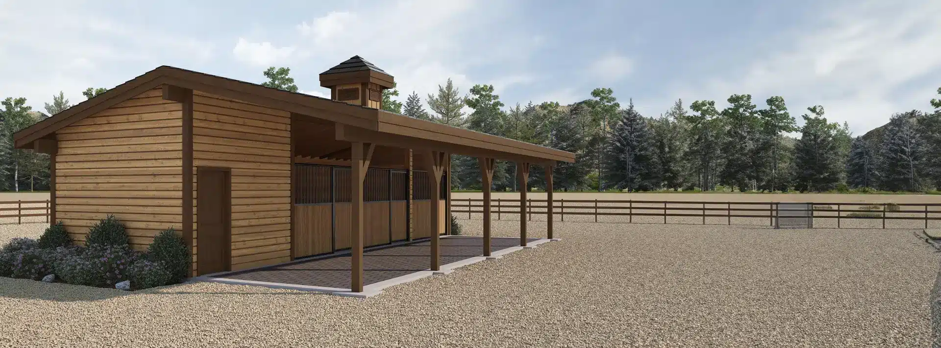 A wooden horse barn with a covered porch stands on a gravel lot, bordered by a wooden fence with trees and a blue sky behind.