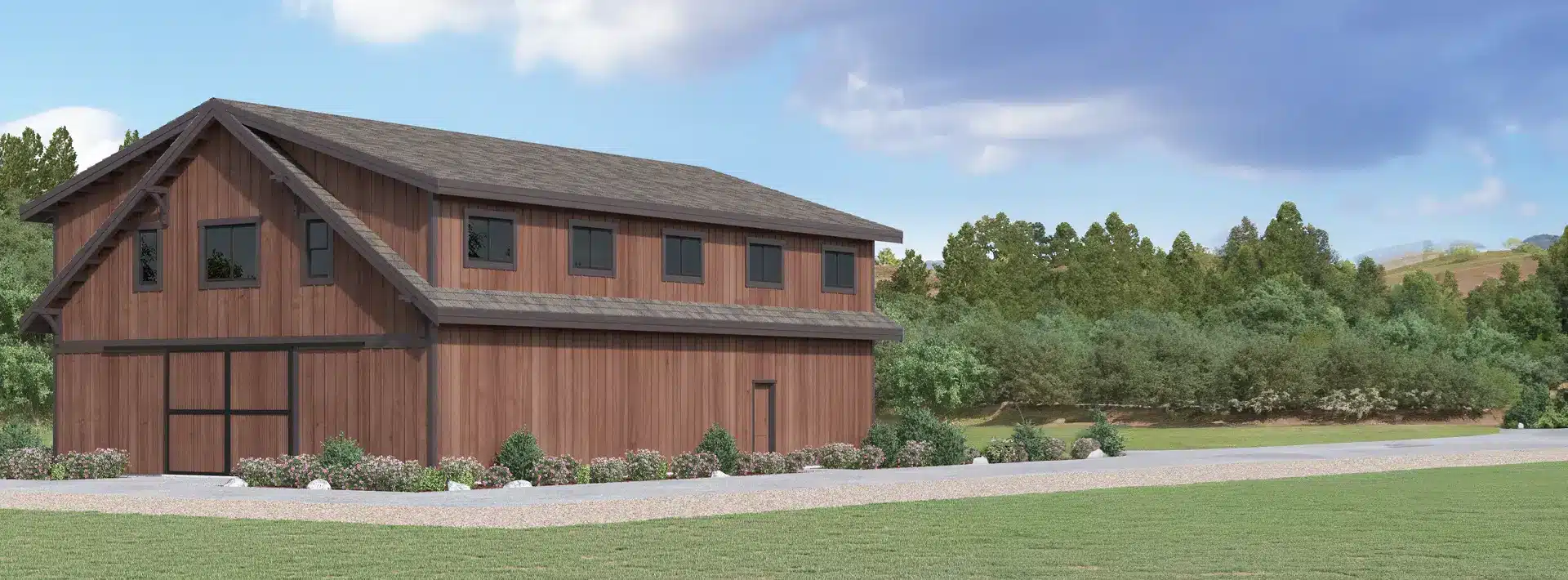 A large brown wooden barn with a gabled roof stands on a manicured lawn, surrounded by green trees and shrubs under a partly cloudy sky.