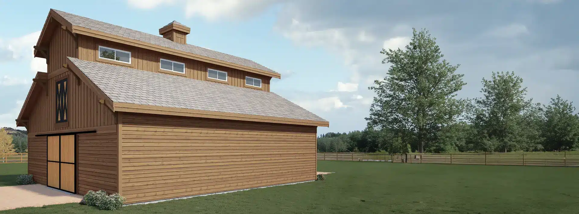 A large wooden barn with a peaked roof and cupola sits on a grassy field, surrounded by a fence and trees under a partly cloudy sky.