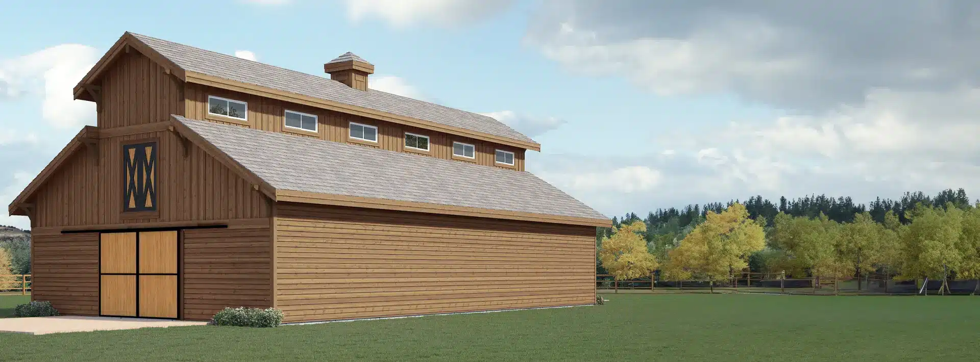 A large wooden barn with a peaked roof, wide double doors, and several windows stands on grass. Trees and a fence are behind it.