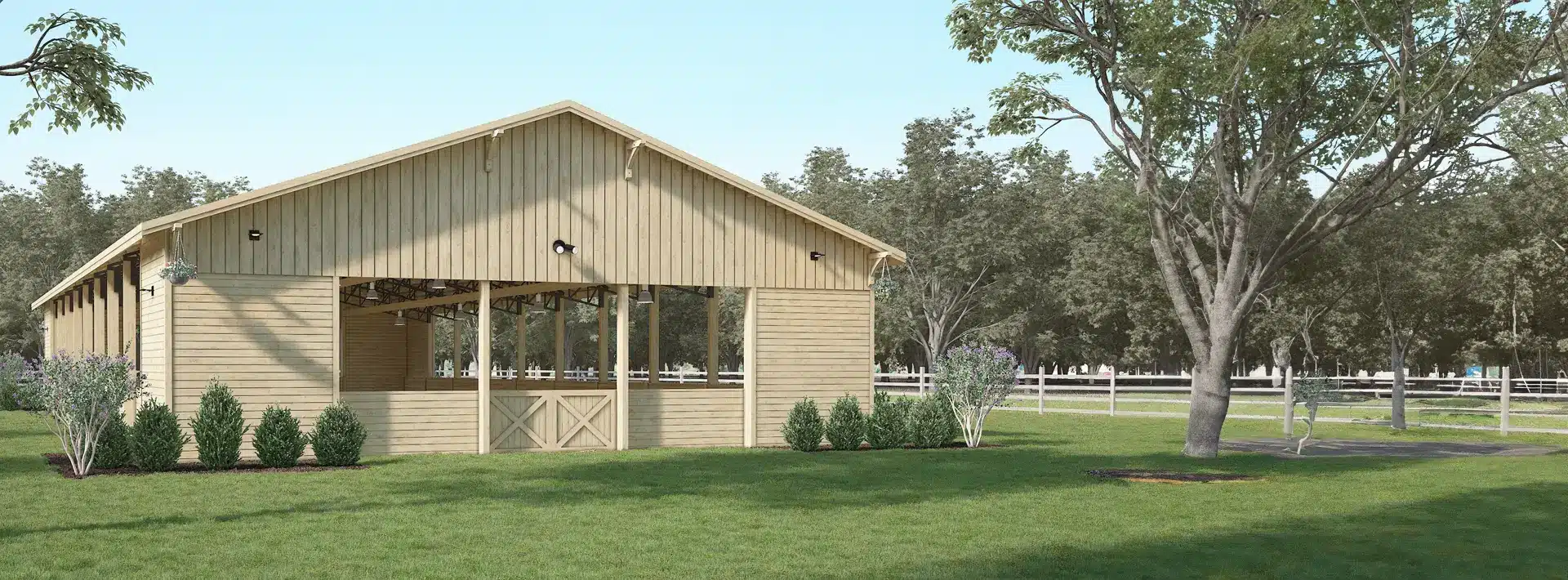 A wooden barn with open sides stands on a grassy field, surrounded by trees, shrubs, and a white fence under a clear sky.