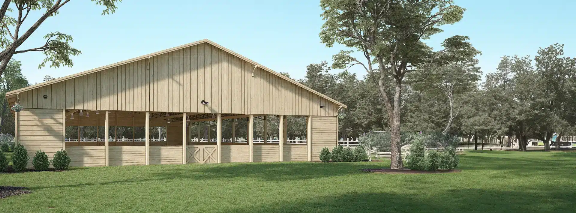 A large wooden barn with open sides stands on a manicured lawn, surrounded by trees and shrubs, under a clear blue sky.