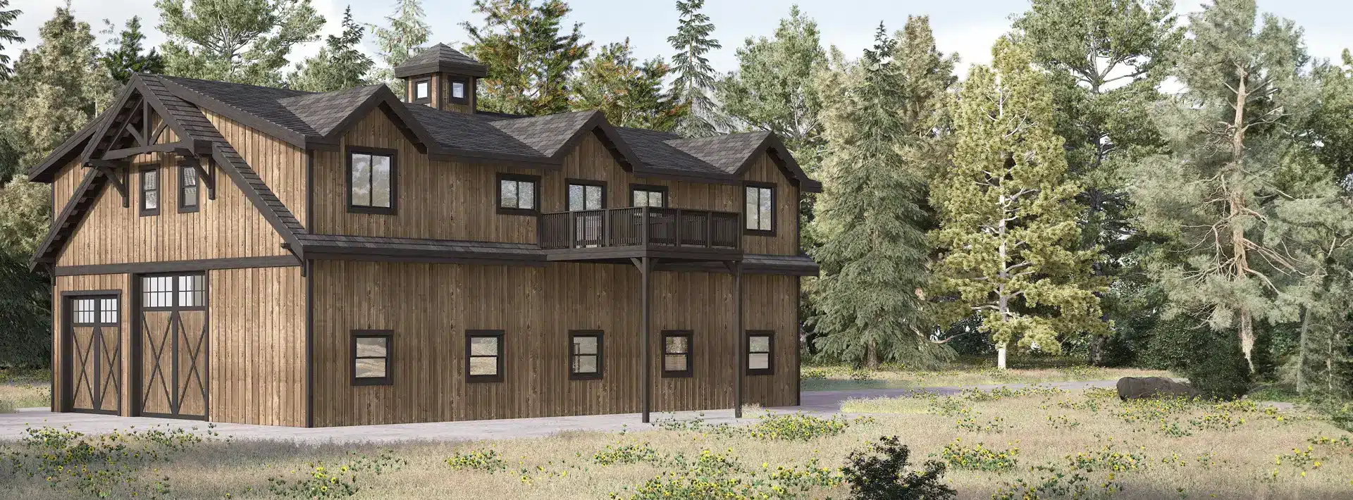A two-story post and beam barn-style house with dark trim and a balcony, surrounded by trees and wildflowers in a grassy clearing.