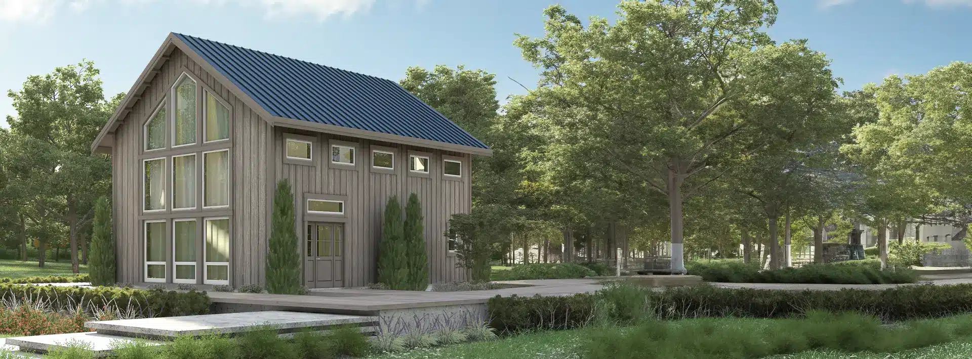 A small modern wooden house with large windows and a blue metal roof stands among green trees and landscaped grass under a sunny sky. Steps and shrubs accent the front entry.