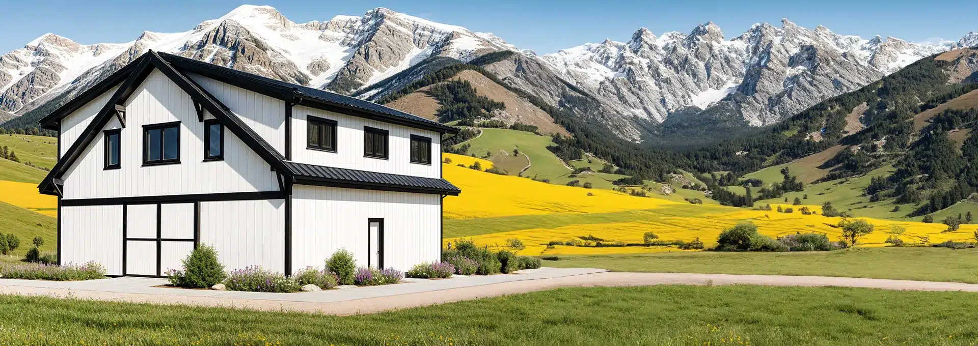 A modern white house with black trim sits in a field of yellow wildflowers, surrounded by hills and snow-capped mountains under a blue sky.