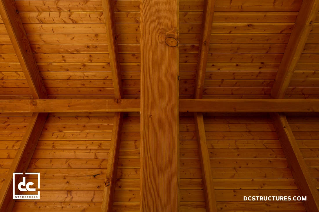 View of a wooden ceiling with exposed beams and tongue-and-groove planks, photographed from below.