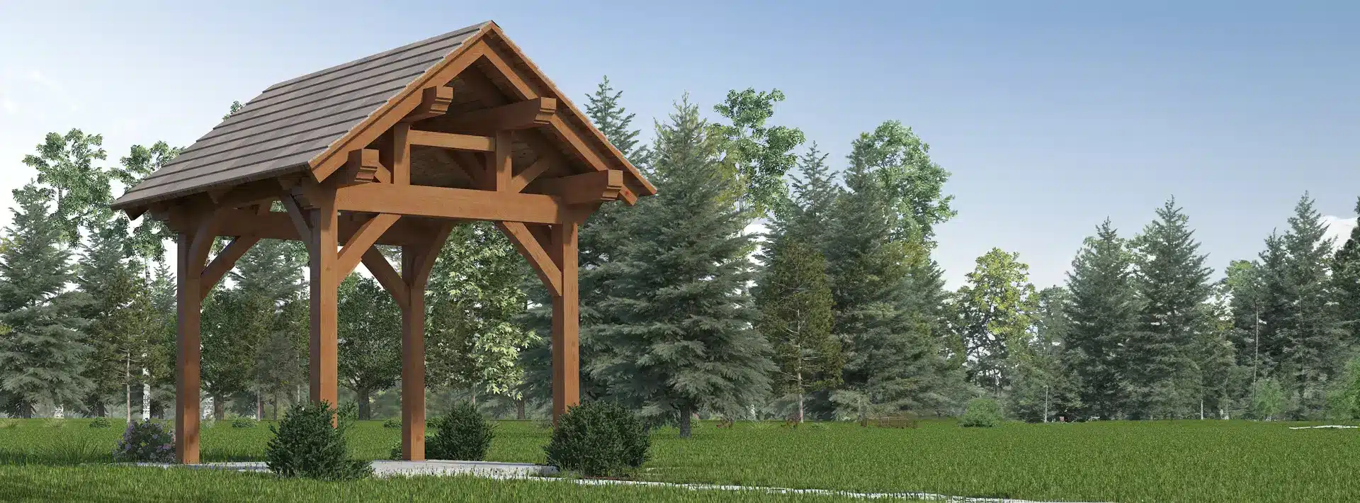 A wooden pavilion with a pitched roof stands on grass, surrounded by bushes and tall evergreens beneath a clear blue sky.