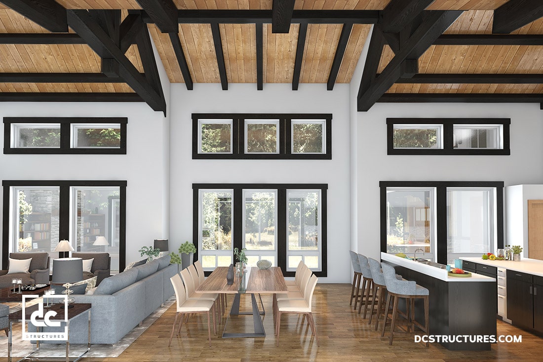 A modern, open-concept living and dining area featuring high ceilings with exposed beams, large windows, and natural lighting. The room includes a gray sectional sofa, a wooden dining table with gray chairs, and a kitchen island with bar stools.