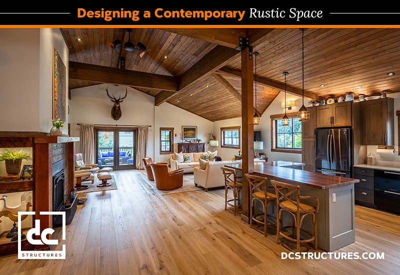 A contemporary rustic living space featuring wooden beams, open layout, cozy seating area, large windows with curtains, mounted deer head, pendant lights, and a kitchen island. Flooring is light wood. Logo reads "DC Structures.