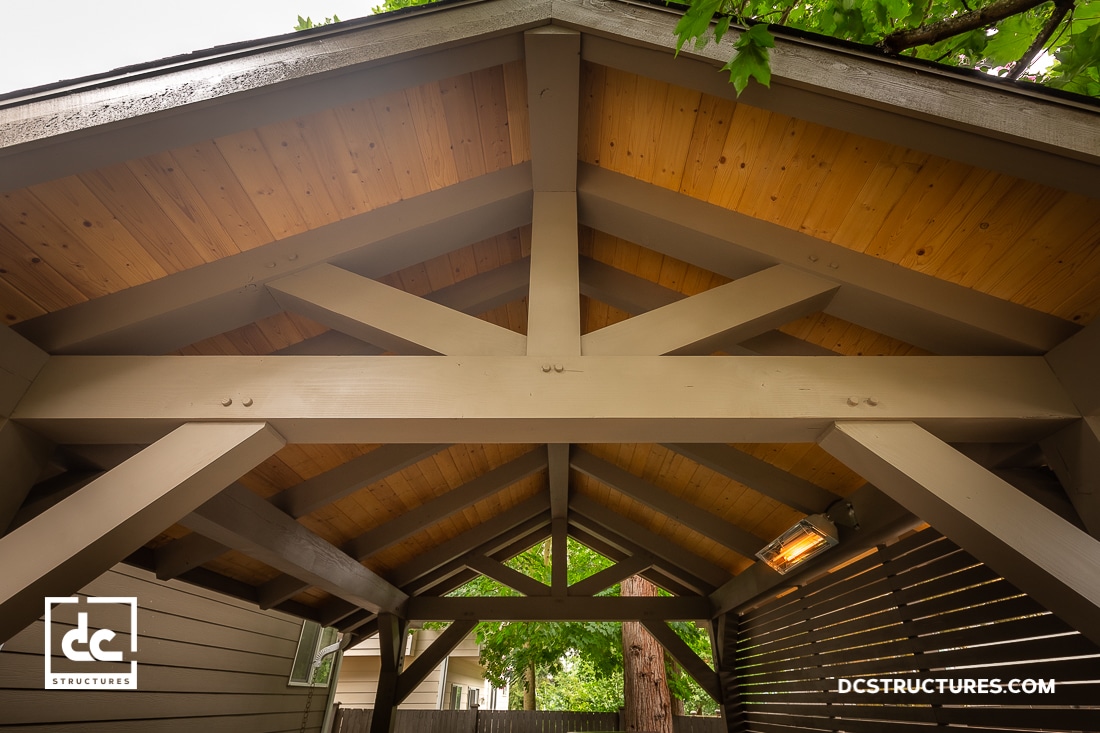 A close-up view of the wooden beams and roof trusses inside a covered outdoor structure, featuring exposed timber framing and a wood-paneled ceiling.