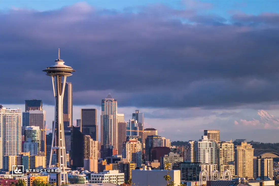 The Seattle skyline featuring the Space Needle in the foreground, with modern skyscrapers under a partly cloudy sky.