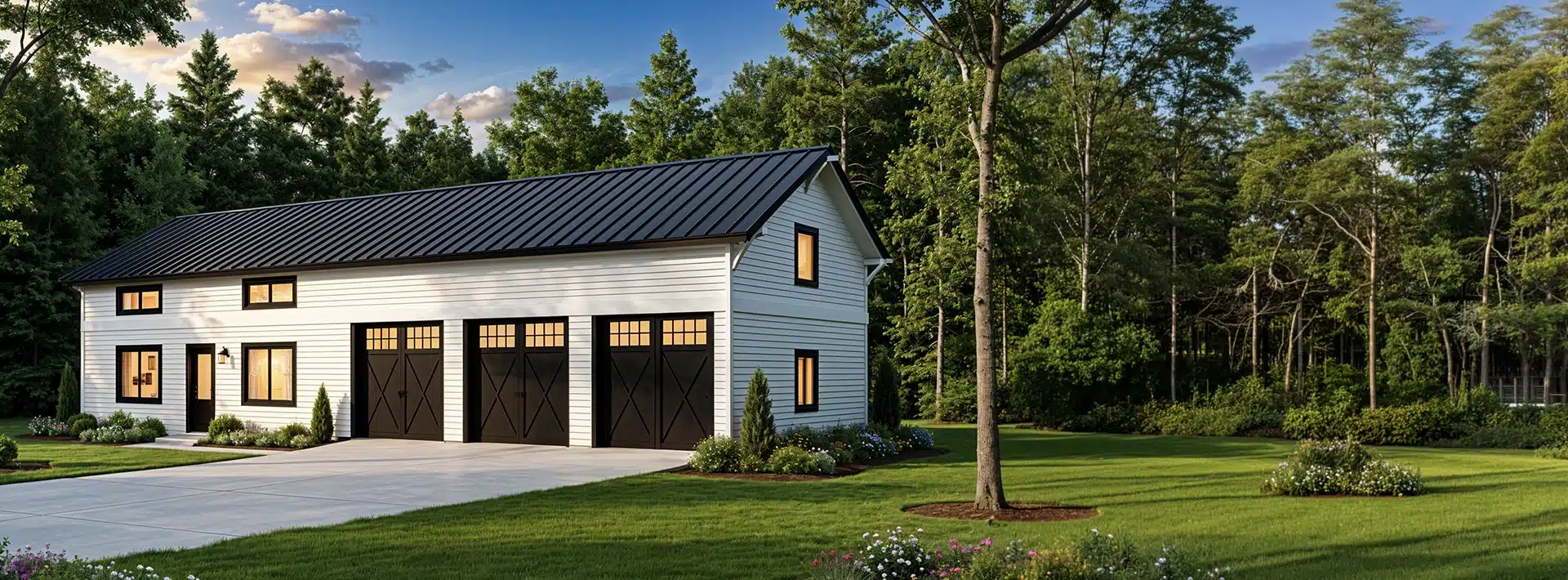 A modern white barn-style house with black trim and three large garage doors beside a green lawn, trees, and flower beds in sunlight.