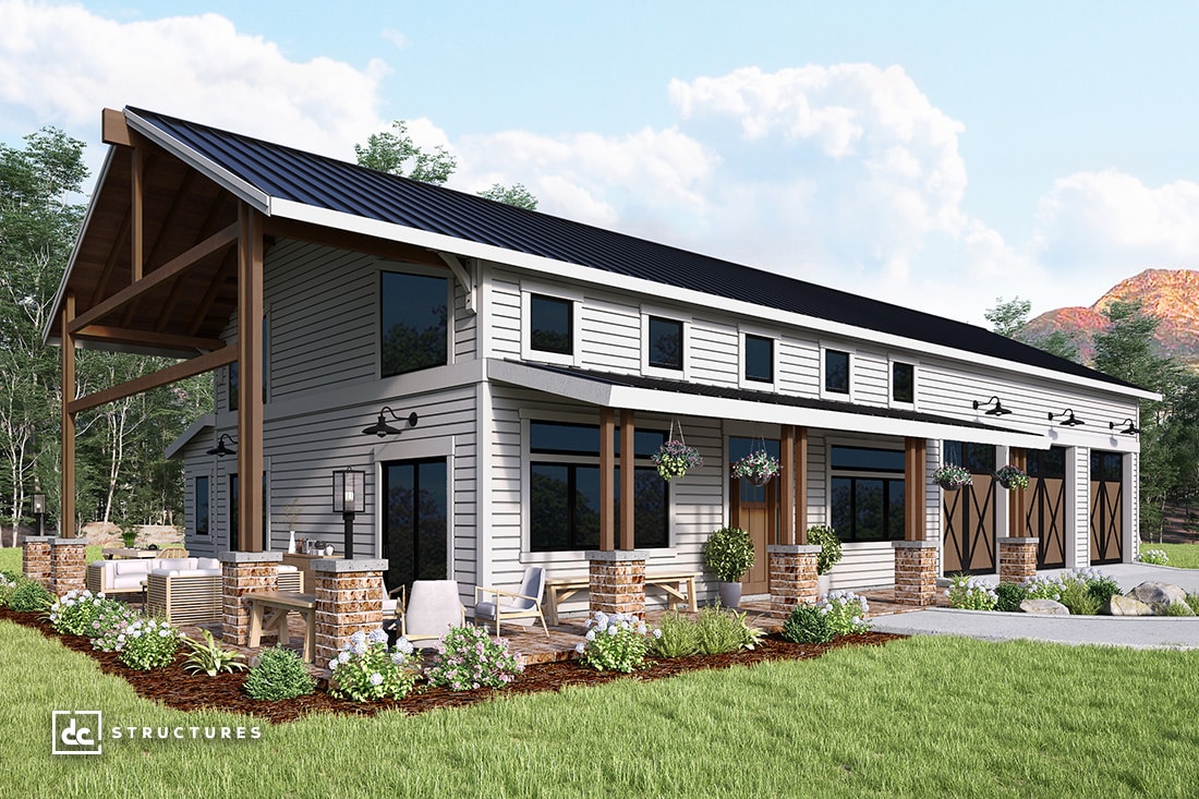 This modern barn-style building, inspired by barndominium kits, features a dark metal roof and white siding. Large windows and wooden accents enhance the design. Outdoor seating and potted plants adorn the spacious patio, surrounded by trees and mountains under a partly cloudy sky.