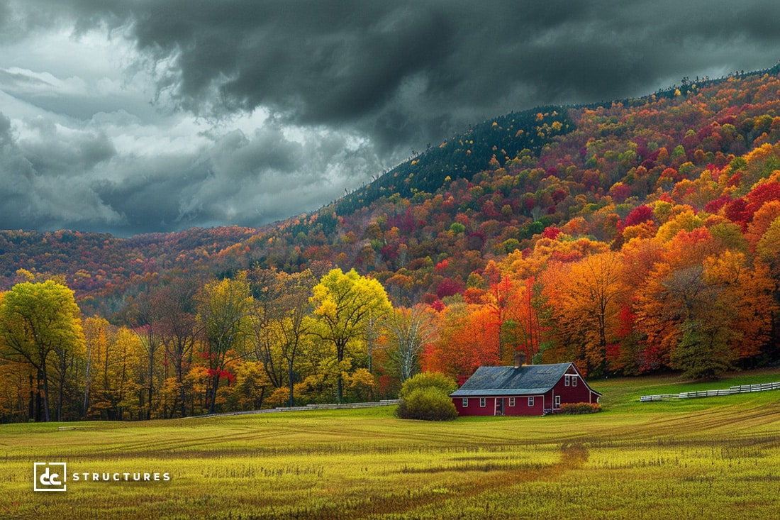 A vibrant autumn landscape features a red barn, reminiscent of modern apartment barn kits, nestled in a green field. Surrounding the barn are colorful trees in shades of red, orange, yellow, and green. In the background, rolling hills are covered with more colorful foliage beneath dramatic, cloudy skies.