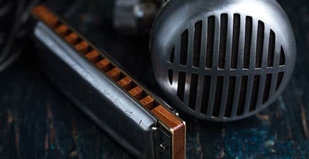 Close-up of a vintage-style microphone next to a harmonica on a dark, textured surface. The microphone features a metallic grille, while the harmonica shows wooden and metal details. Both items suggest a musical theme, reminiscent of blues or rock genres—perfect for jam sessions in cozy apartment barn kits.