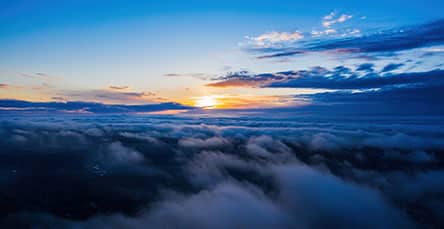 A breathtaking aerial view of a sunrise over a sea of clouds. The sun peeks out from behind the horizon, casting warm orange and golden hues across the sky, while the clouds below appear soft and billowy, creating a serene and ethereal atmosphere, reminiscent of peaceful mornings near apartment barn kits.