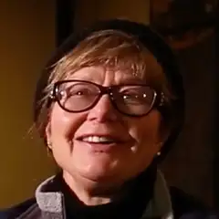 A person with glasses and a beanie is smiling in a warmly lit indoor setting.