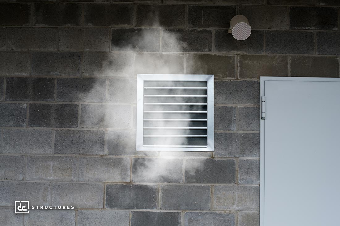 A vent on a gray brick wall emits a cloud of steam or smoke. A closed door is adjacent. The logo dc STRUCTURES is in the bottom left corner.