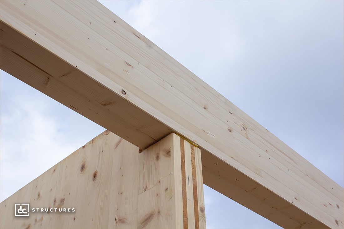 Close-up view of light wooden beams intersecting under a cloudy sky. The beams show a smooth texture with visible wood grains and knots.