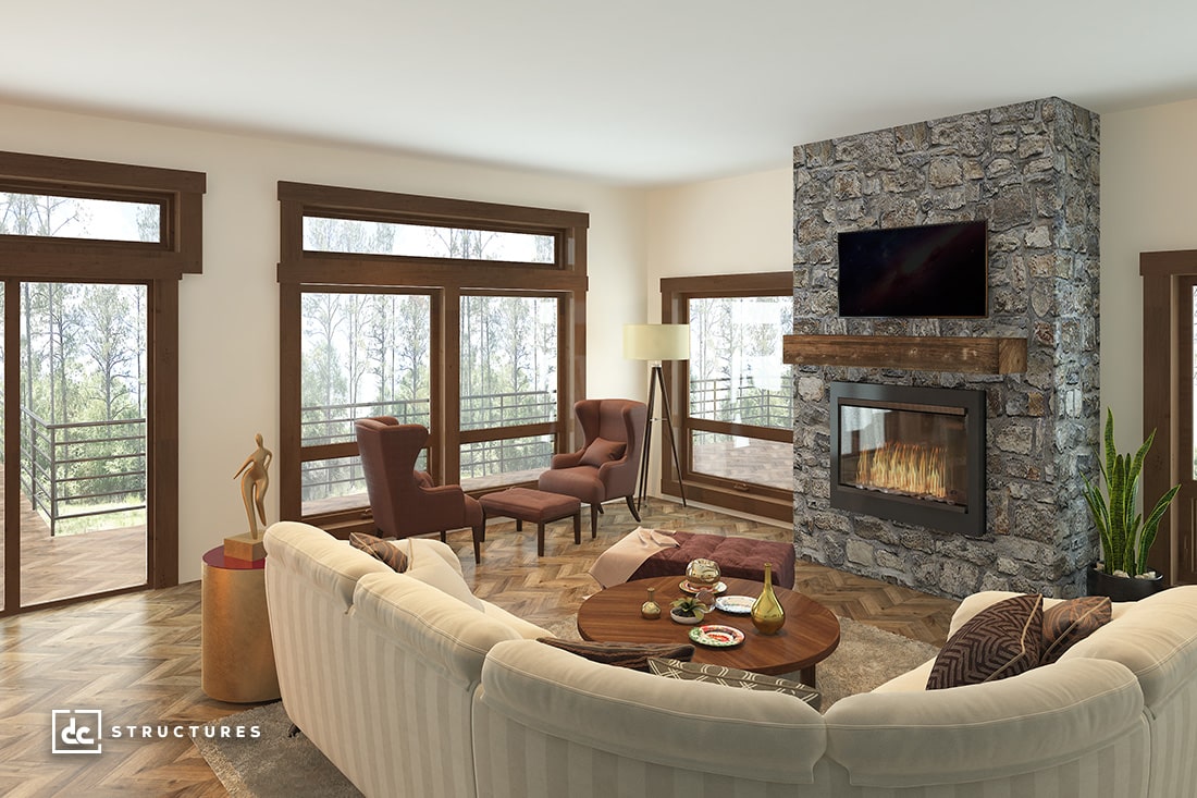 A cozy living room with a stone fireplace and a wall-mounted TV. A round coffee table is surrounded by a curved beige sofa and two brown armchairs. Large windows showcase a wooded view. A tall lamp and a sculpture are also visible.