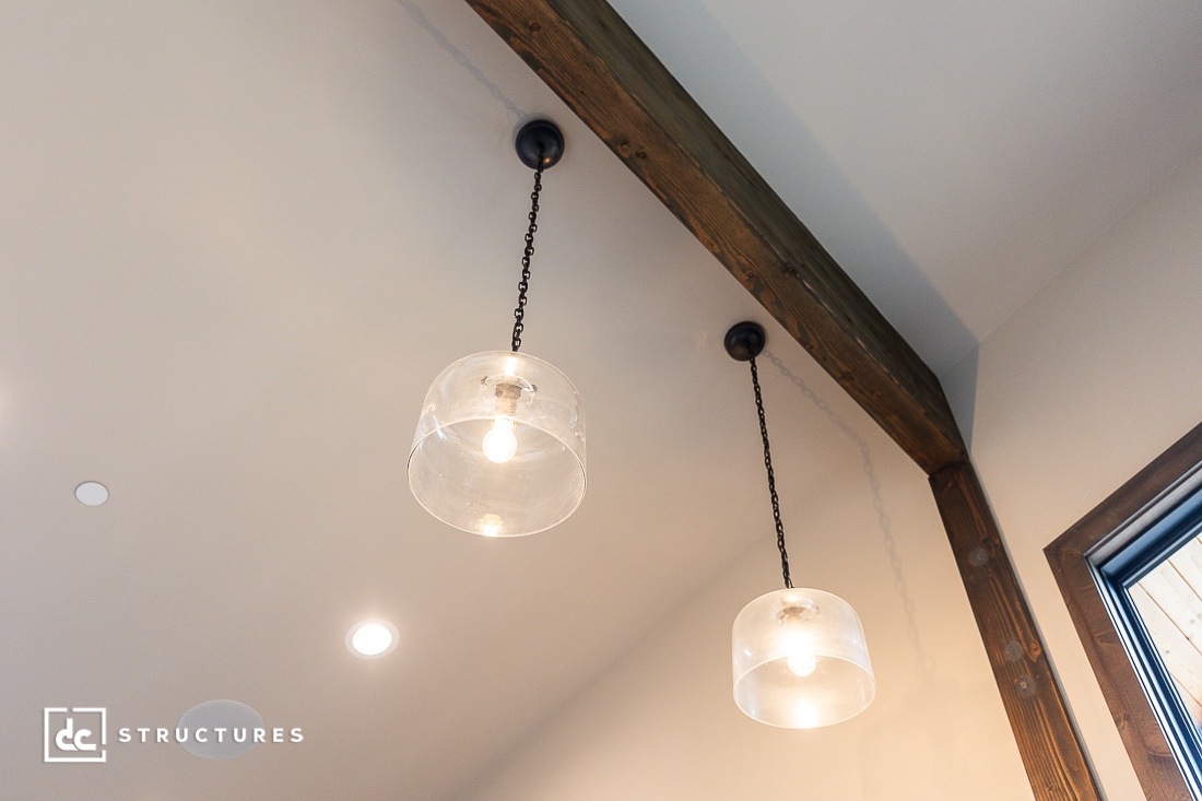 Two hanging pendant lights with clear glass shades are suspended from the ceiling by dark chains. The ceiling is light-colored with a wooden beam and a nearby recessed light.