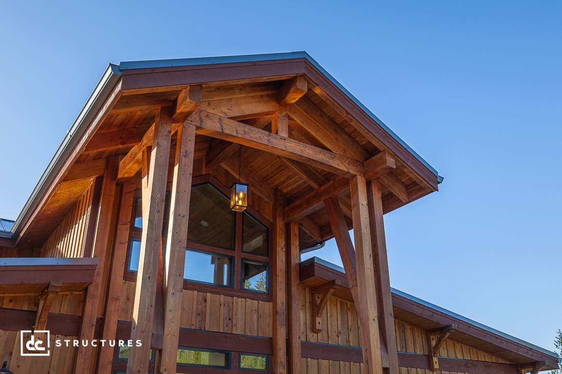 A close-up view of a timber-framed building with tall wooden beams, large windows, and a hanging lantern under the peaked roof.