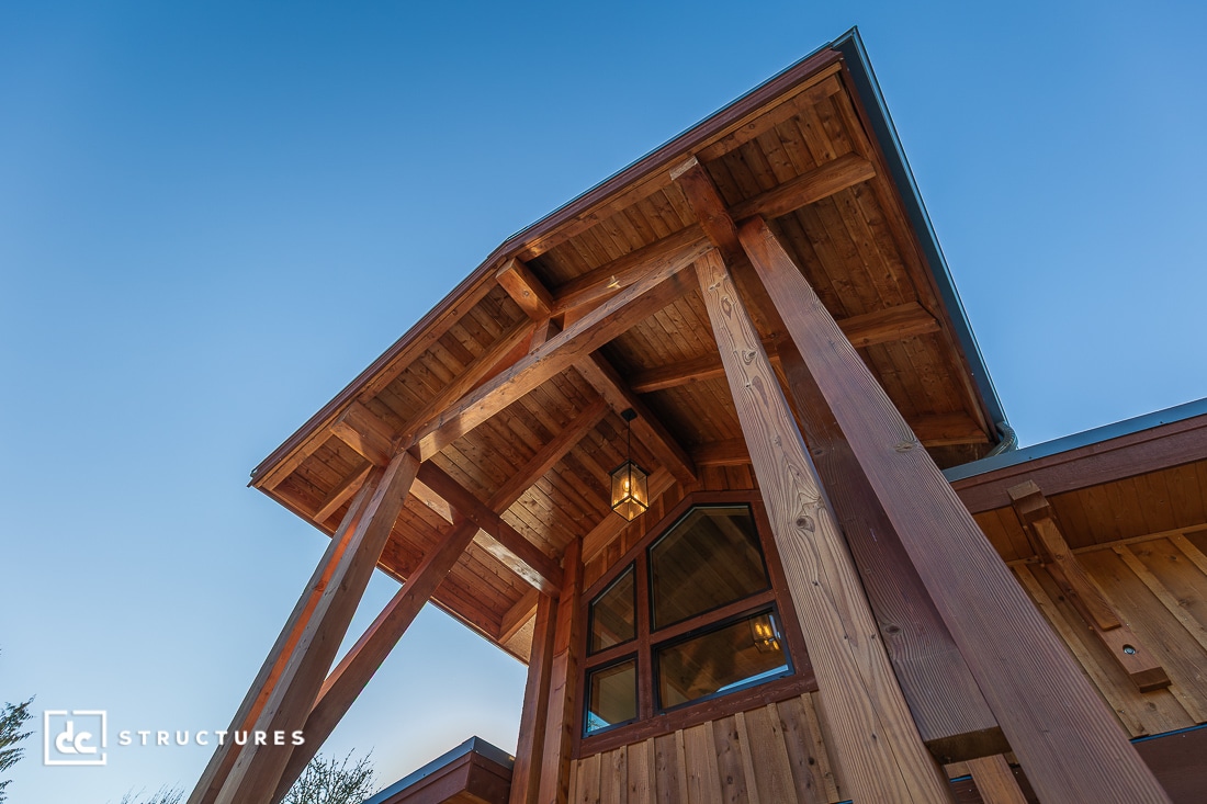 A low-angle view of a timber-framed building entrance with exposed beams, peaked roof, glass windows, and a hanging lantern.