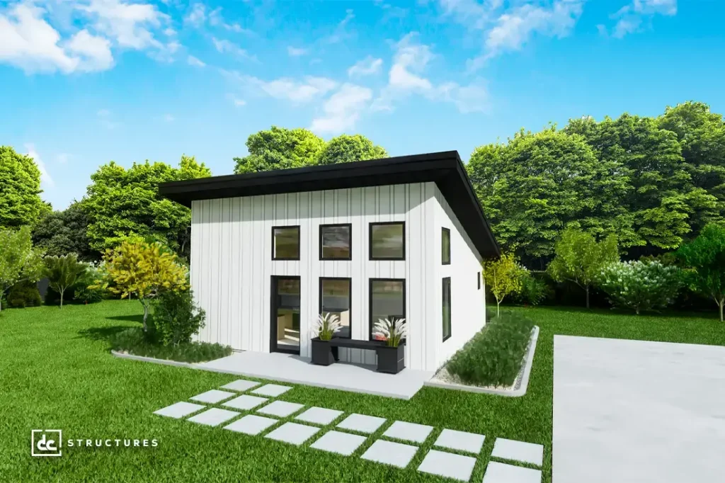 A modern small white house with a slanted black roof, tall windows, green yard, trees, blue sky, and concrete path to the entrance.