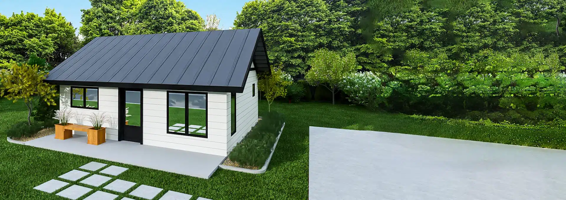 A small, modern white house with a dark metal roof sits on a green lawn with trees, stone pavers, and an empty concrete slab in front.