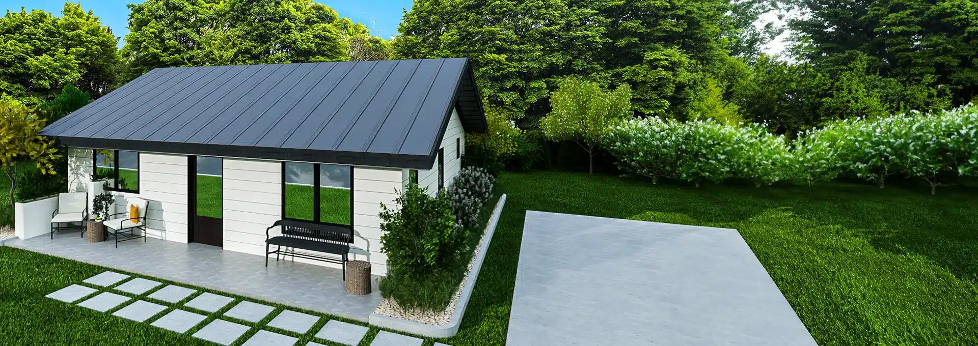 A small modern house with a dark metal roof and large windows sits by a concrete driveway amid lush trees, grass, and shrubs.
