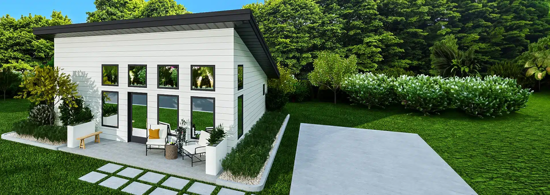 A modern white tiny house with large windows, lush greenery, a small patio with chairs and bench, and a concrete driveway.