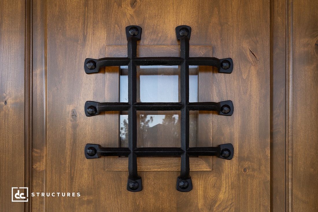A close-up of a wooden door featuring a small square window with black metal bars arranged in a grid pattern.