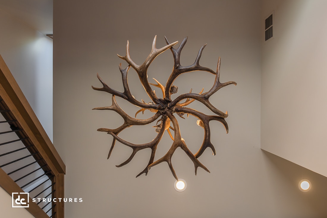 A decorative chandelier made of intertwined antlers hangs from a high ceiling, with light bulbs nestled among the antlers.