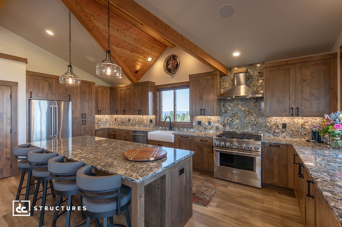A spacious modern kitchen with wood cabinets, marble countertops, a large island, stainless steel appliances, and pendant lights.
