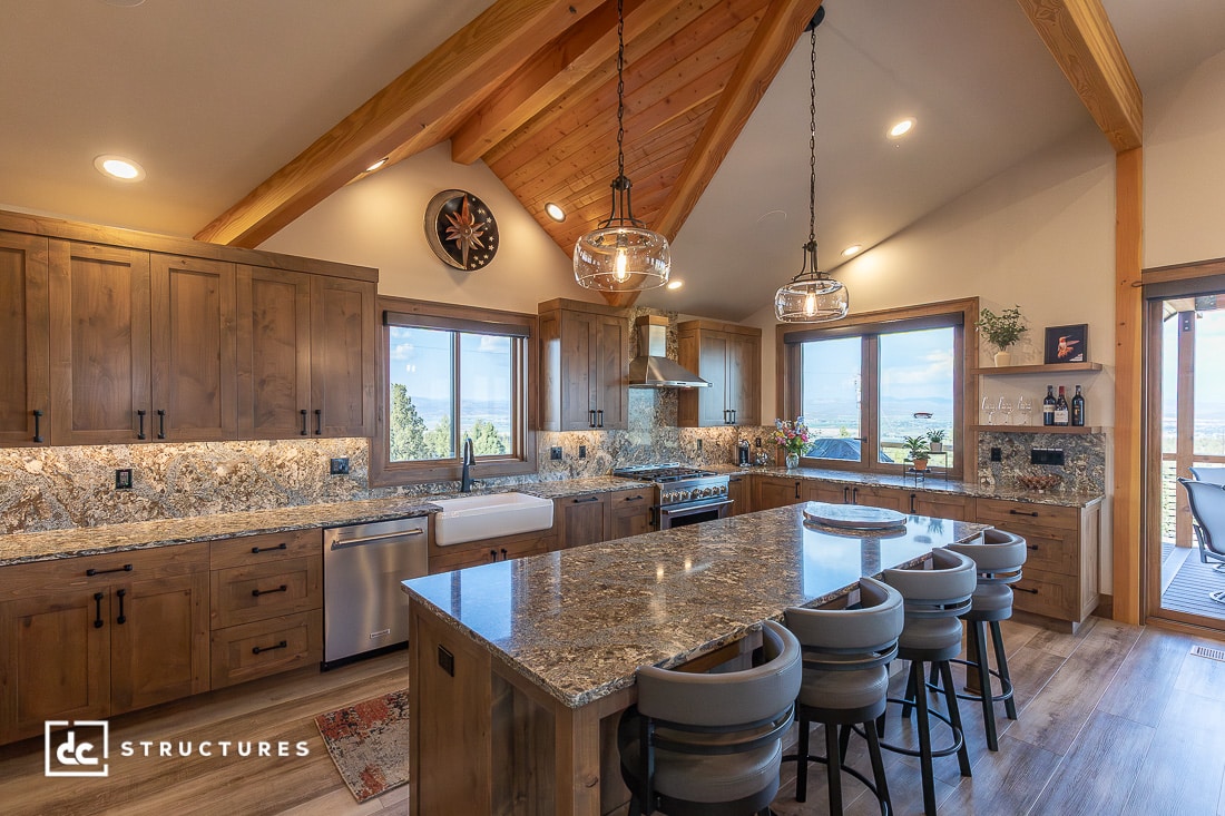 Spacious rustic kitchen with wood cabinets, granite countertops, island with barstools, farmhouse sink, and scenic window views.