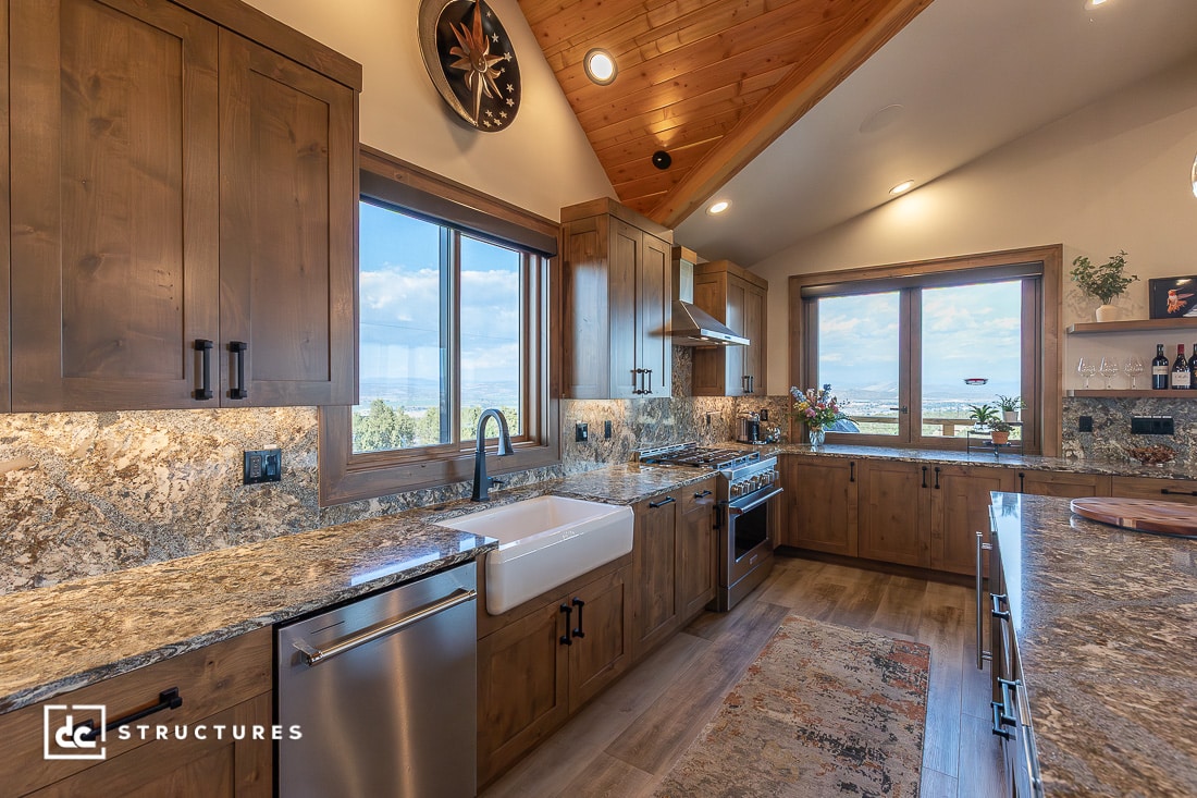 A spacious modern kitchen with wood cabinets, granite countertops, stainless steel appliances, large windows, and a farmhouse sink.