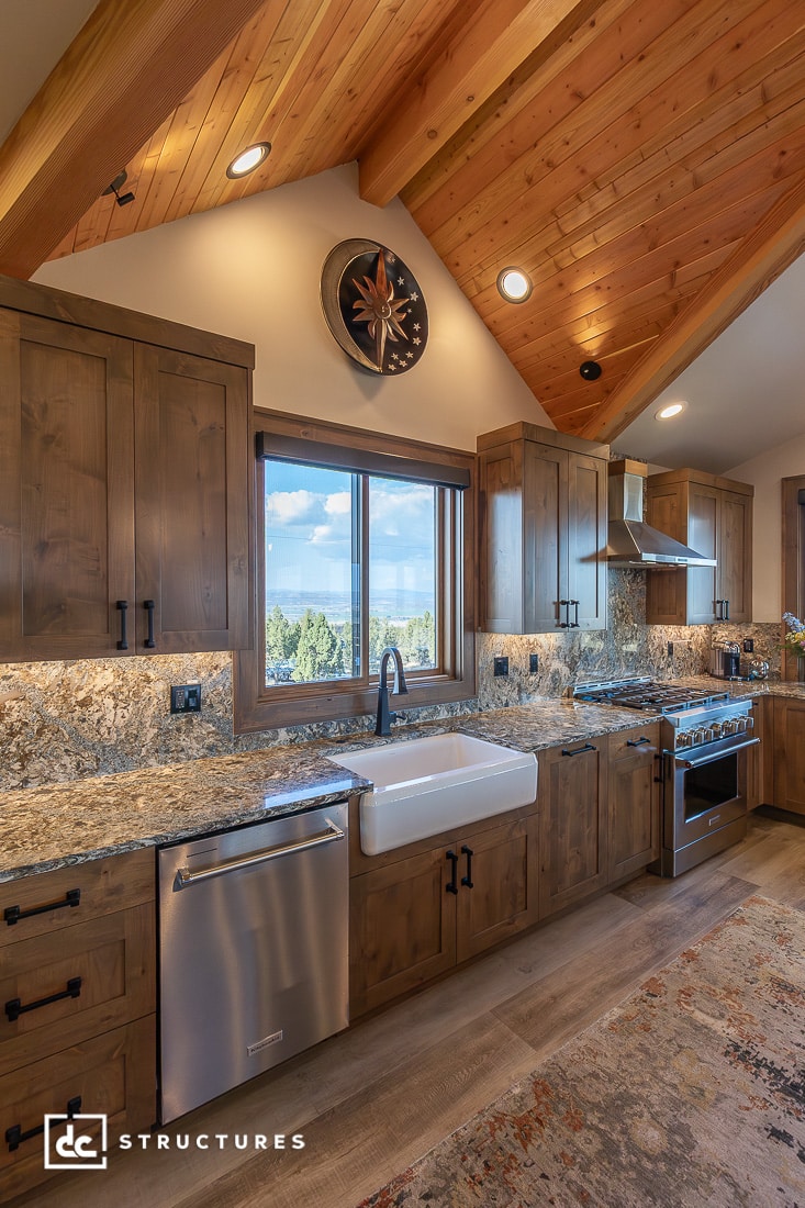 A rustic kitchen with wood cabinets, farmhouse sink, stainless steel appliances, granite countertops, and a window view.