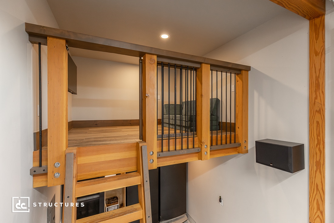 A wooden loft area with a ladder, vertical metal railings, open space above, shelves and storage below, modern lighting, and a small sofa.