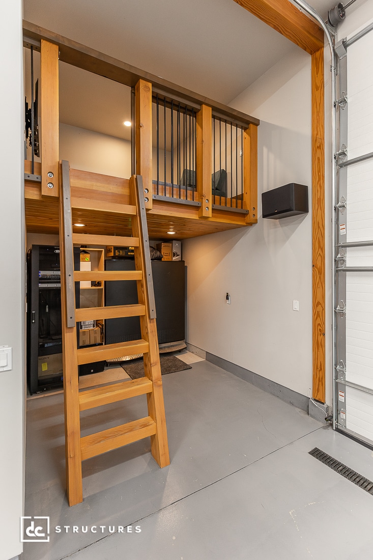 A wooden ladder leads to a loft with railing inside a garage, featuring storage items, appliances, wood beams, and open door.