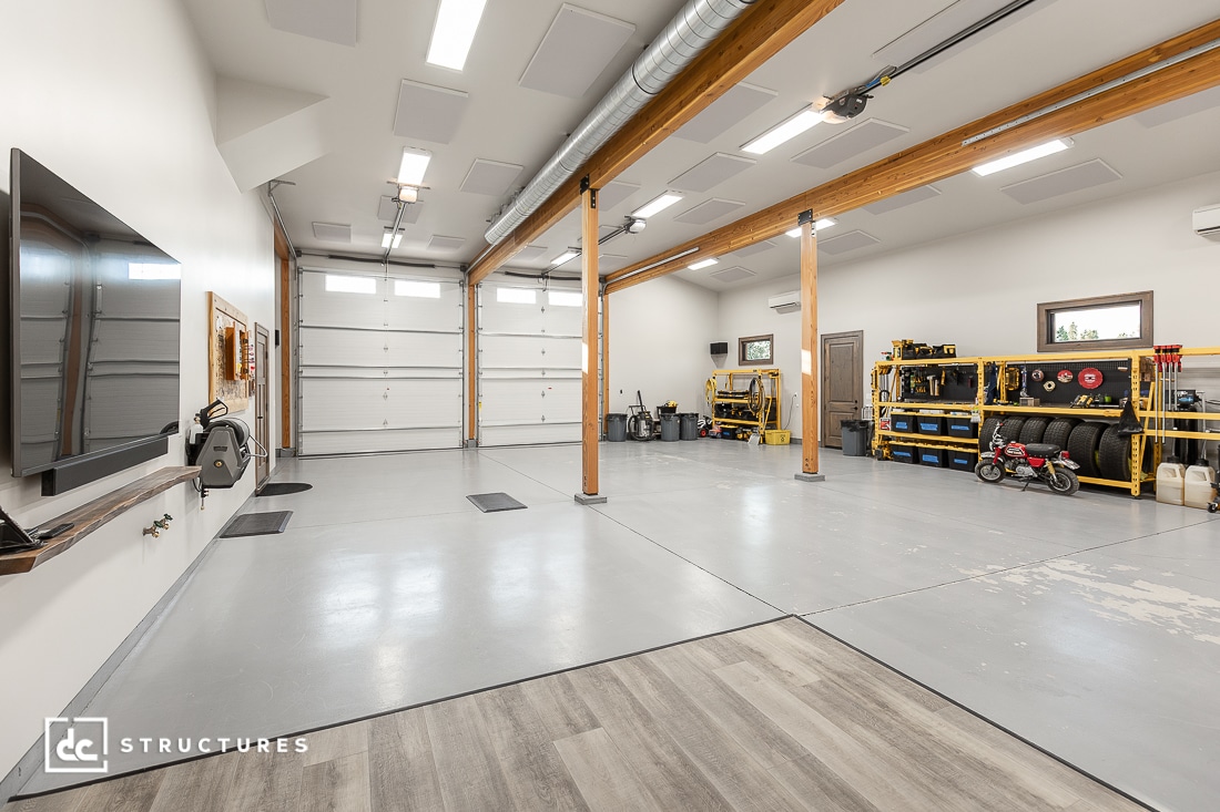A spacious, clean garage with polished concrete floors, wooden beams, storage shelves, tools, and a children's toy motorcycle.