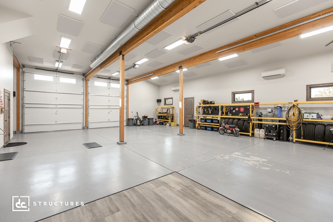 A spacious, clean garage with high ceilings, large windows, double doors, exposed wooden pillars, organized shelves, and a small children's bike.